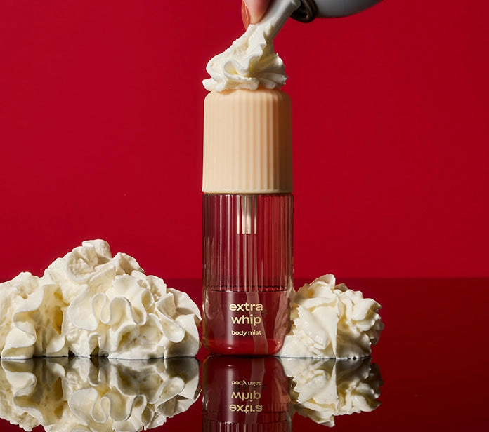 A body mist bottle topped with whipped cream on a red backdrop