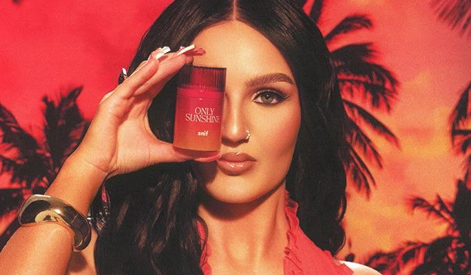 A woman holding a small fragrance bottle in front of one eye
