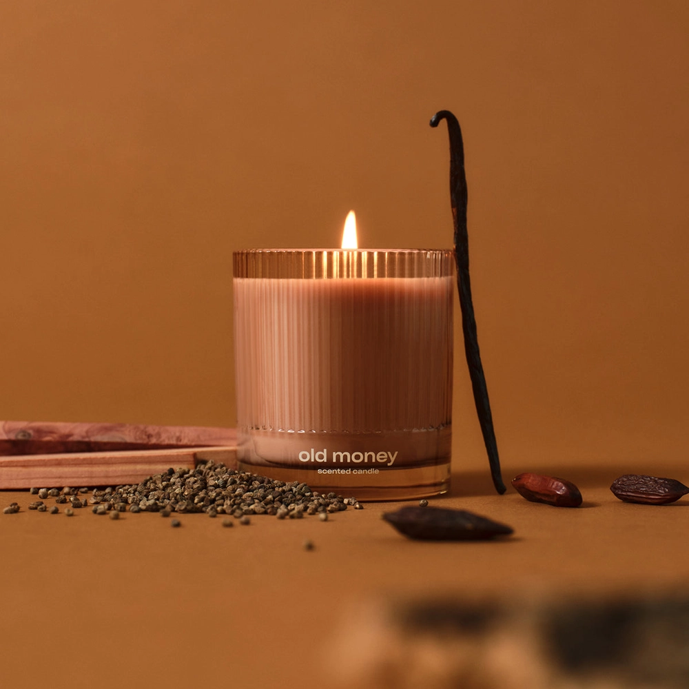 Old Money candle with a vanilla pod on a warm brown backdrop